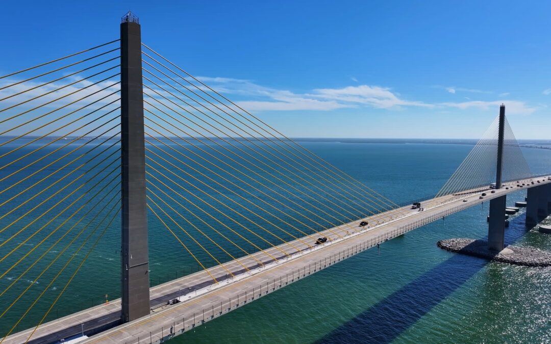 A cable-stayed bridge spans blue water, with vehicles traveling across the deck beneath tall pylons.